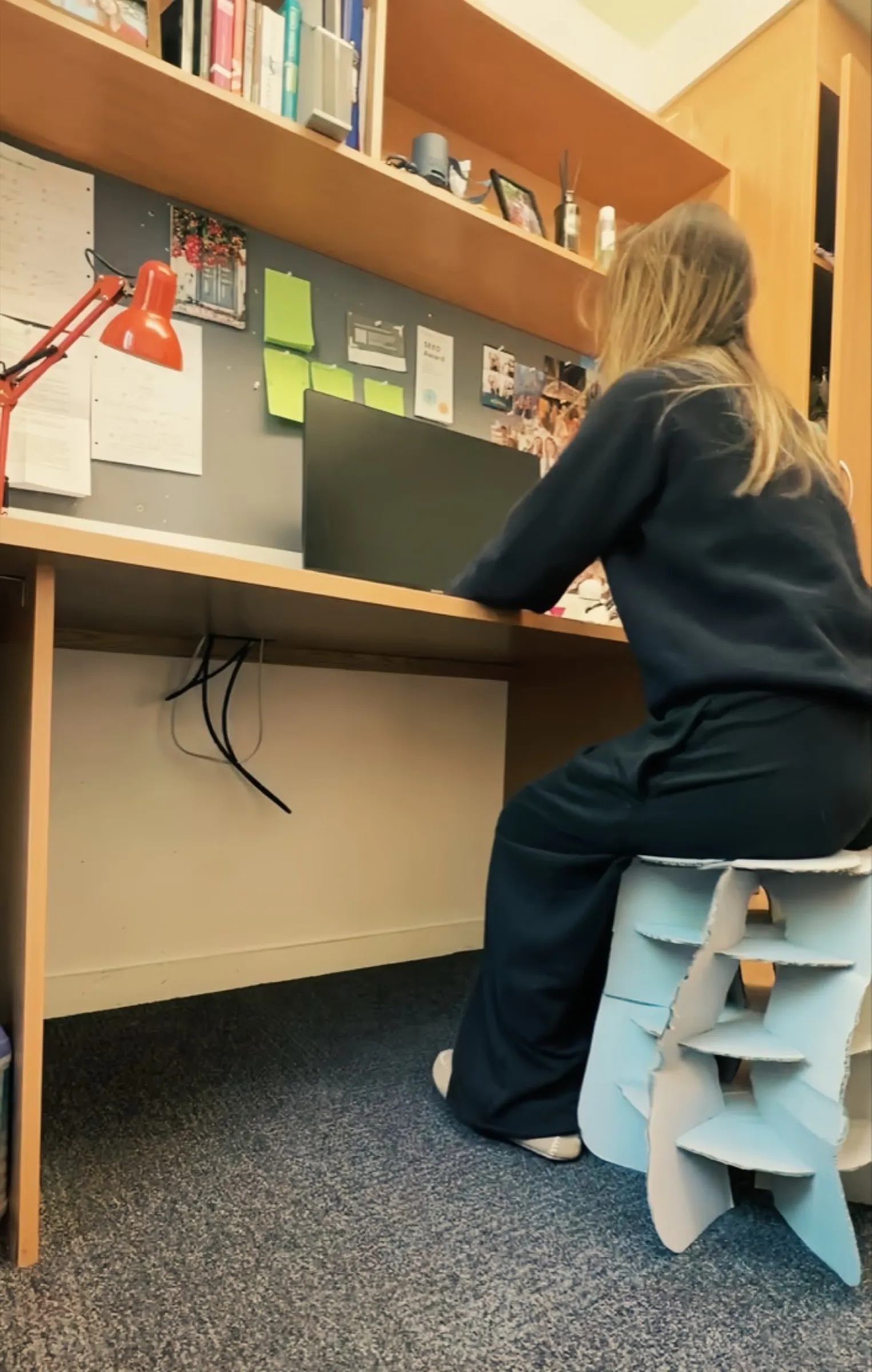 Me sitting on the stool at a desk under a bookshelf, working on a laptop.