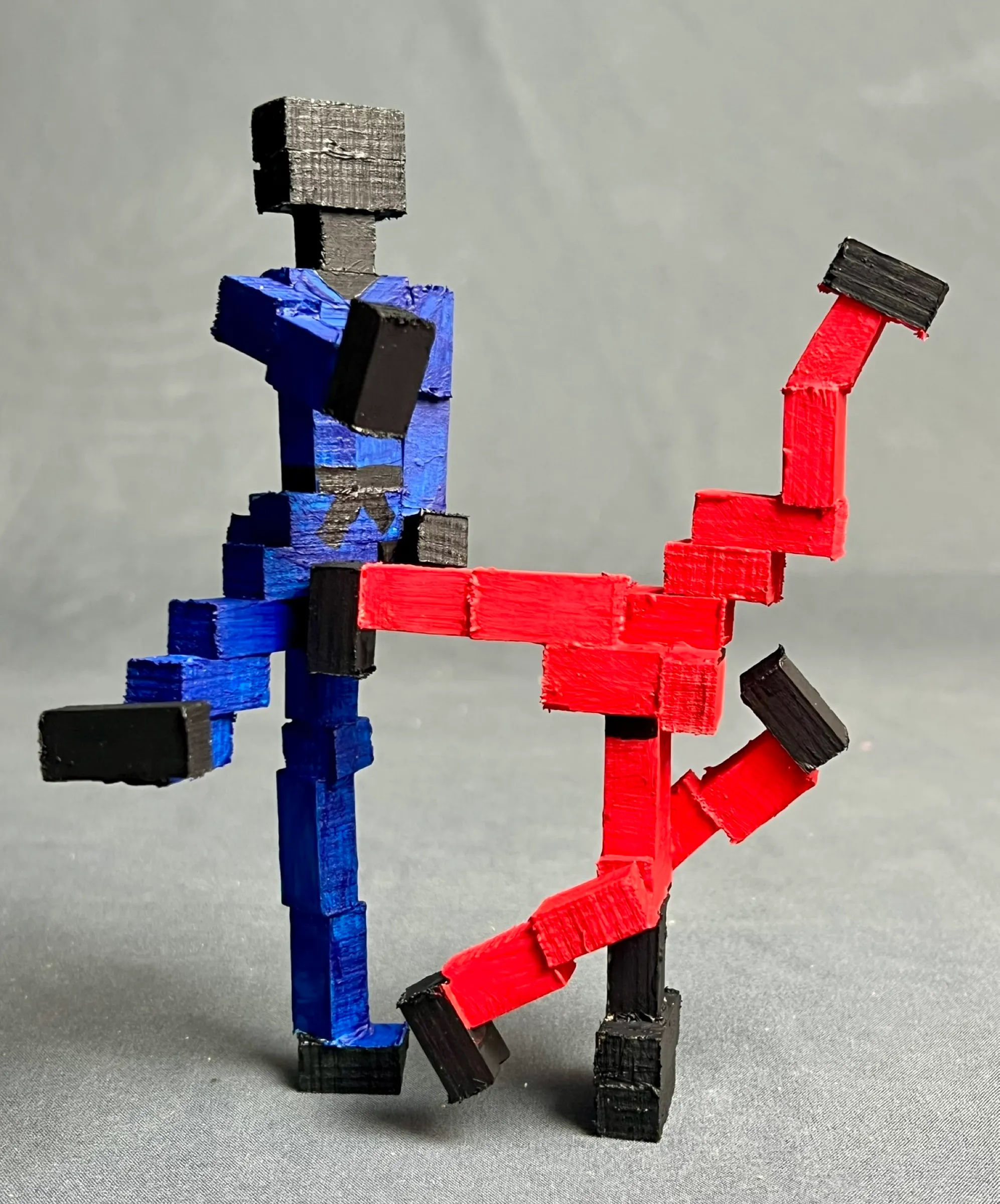 The finished piece from the front: a blue block figure stands on one leg as the red figure, hooked under its arm, swings over with both legs off the ground.