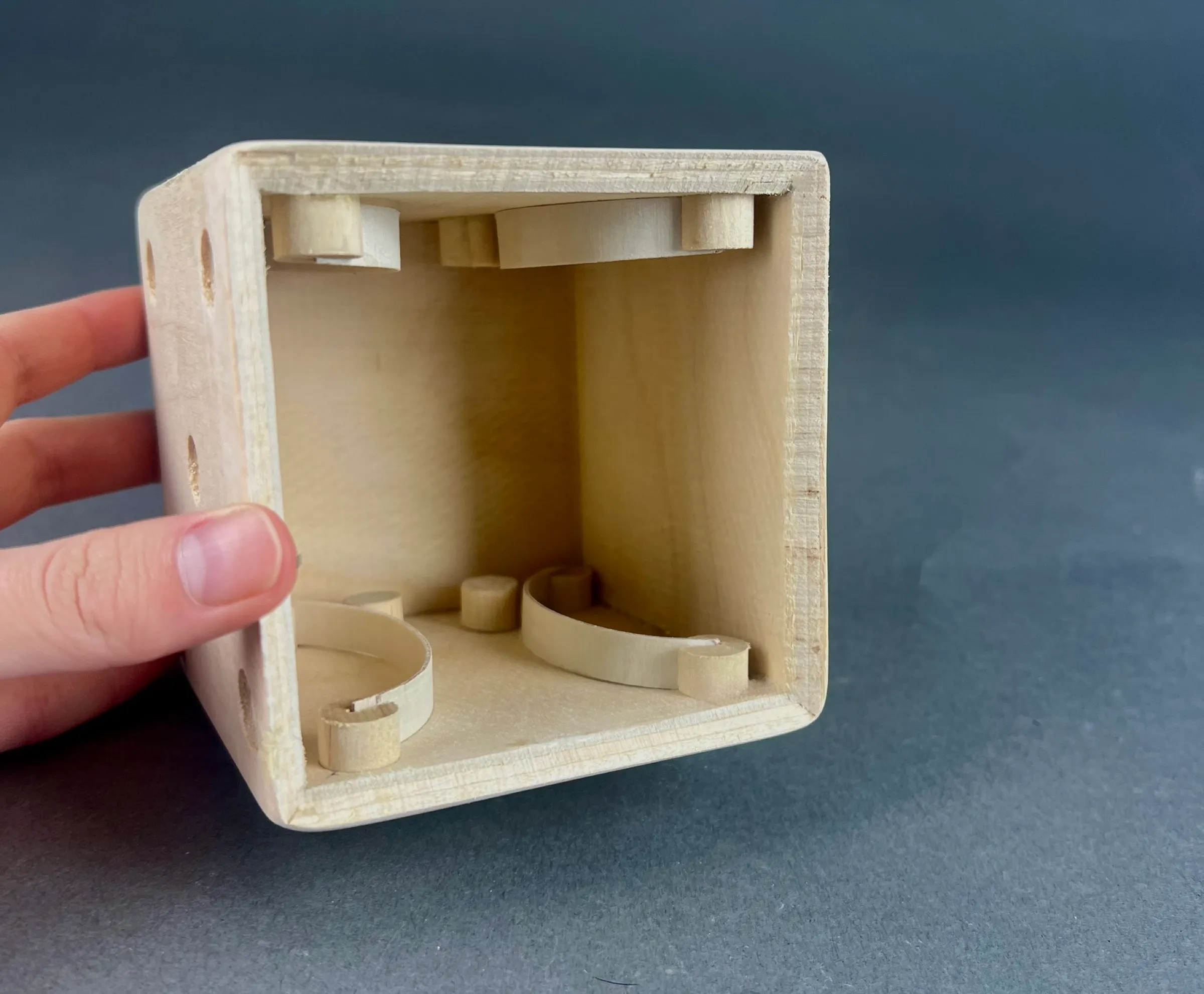The die held open on its side, showing the hidden chamber inside, with the curved spring arms and dowel stoppers at the top and bottom.