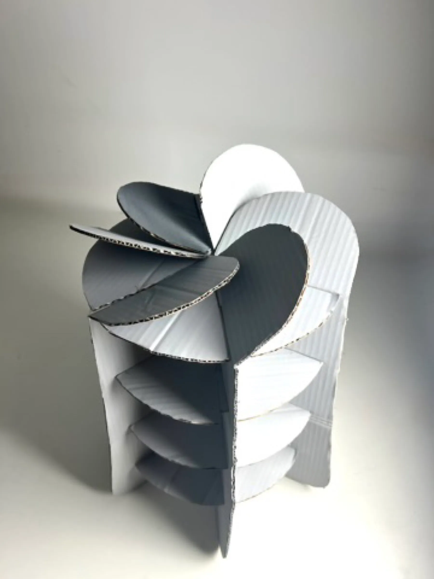 The finished stool in grey card, with grey and white petals on top, against a white wall.