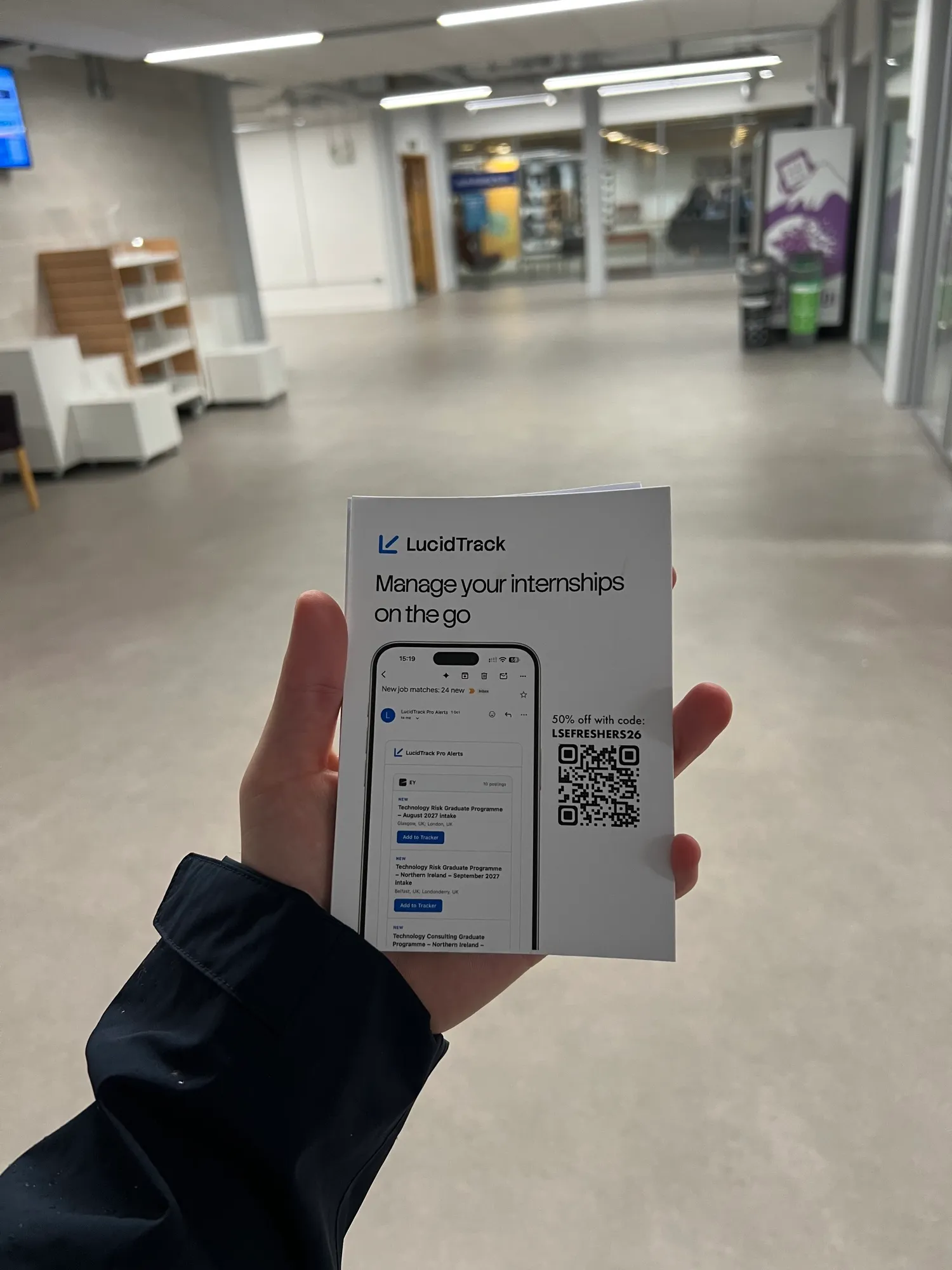 A hand holding a LucidTrack flyer in a university corridor.
