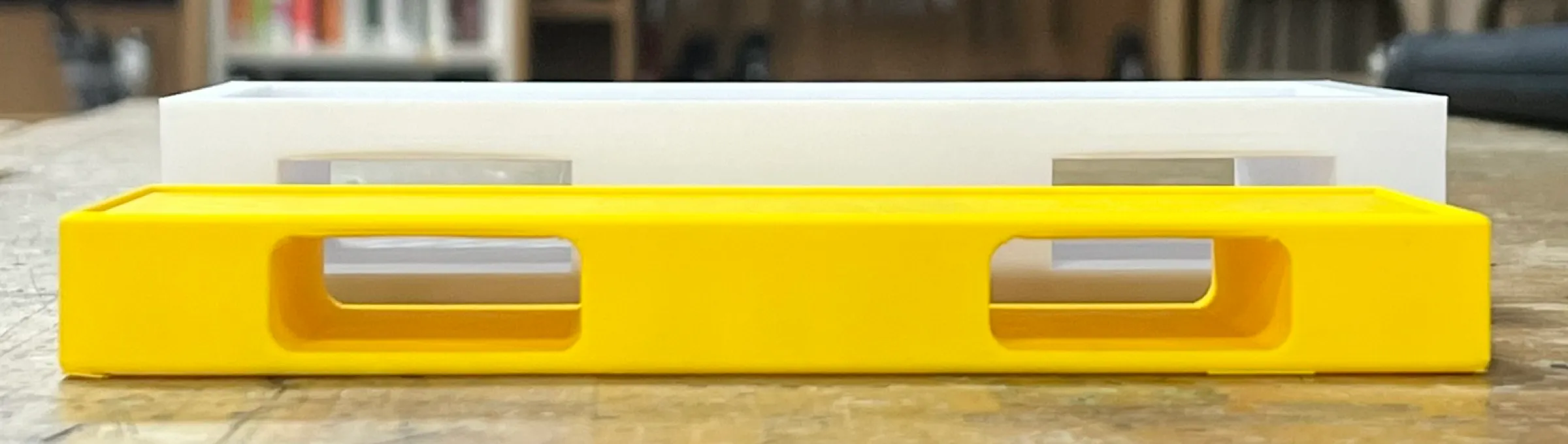 A long yellow 3D-printed housing on a workbench, with two cut-outs along its side for the strap.