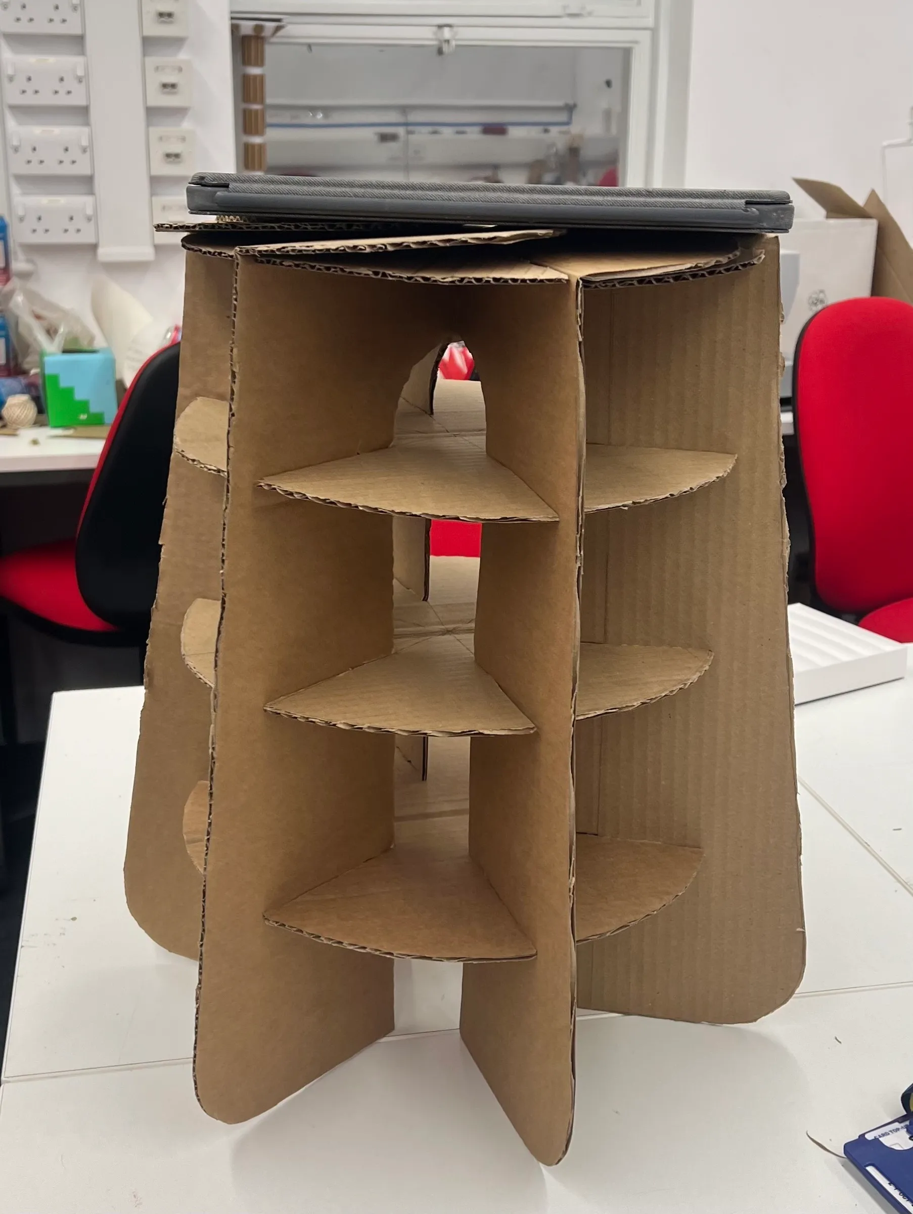 A brown cardboard model of the stool on a studio table, a laptop resting on its seat.
