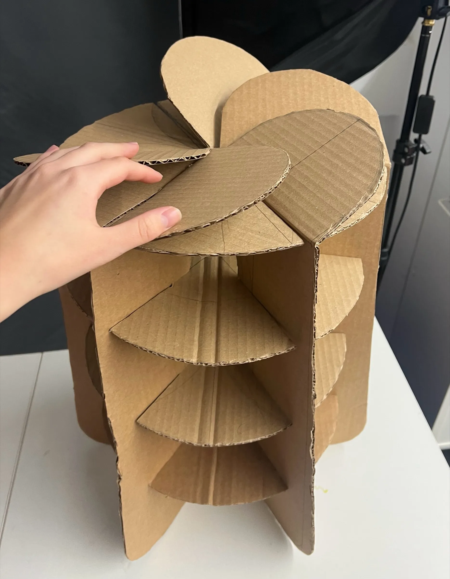 A hand placing the petal-shaped seat pieces on top of a brown cardboard model.