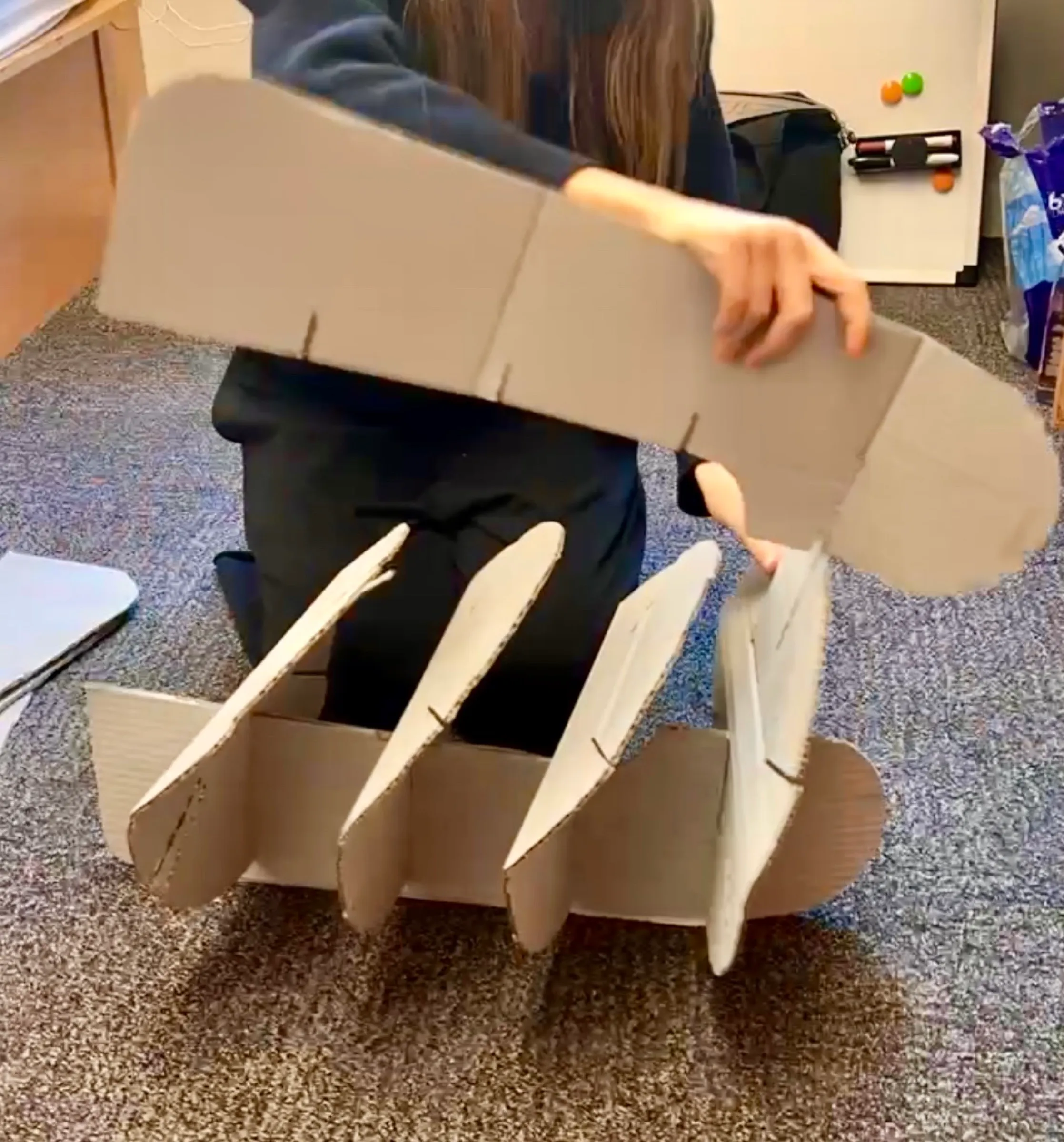 Me lifting a long cardboard part out of a half-assembled model, its slotted fins standing up from the base.
