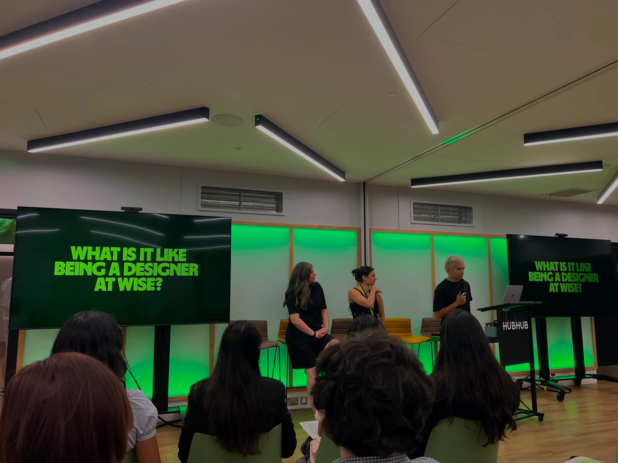 A design panel on stage under green light, the screens asking: what is it like being a designer at Wise?