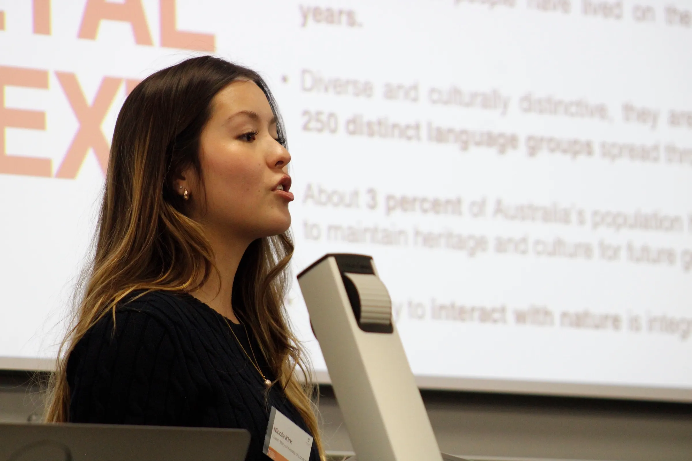 Me presenting at a lectern, the societal context slide behind me.