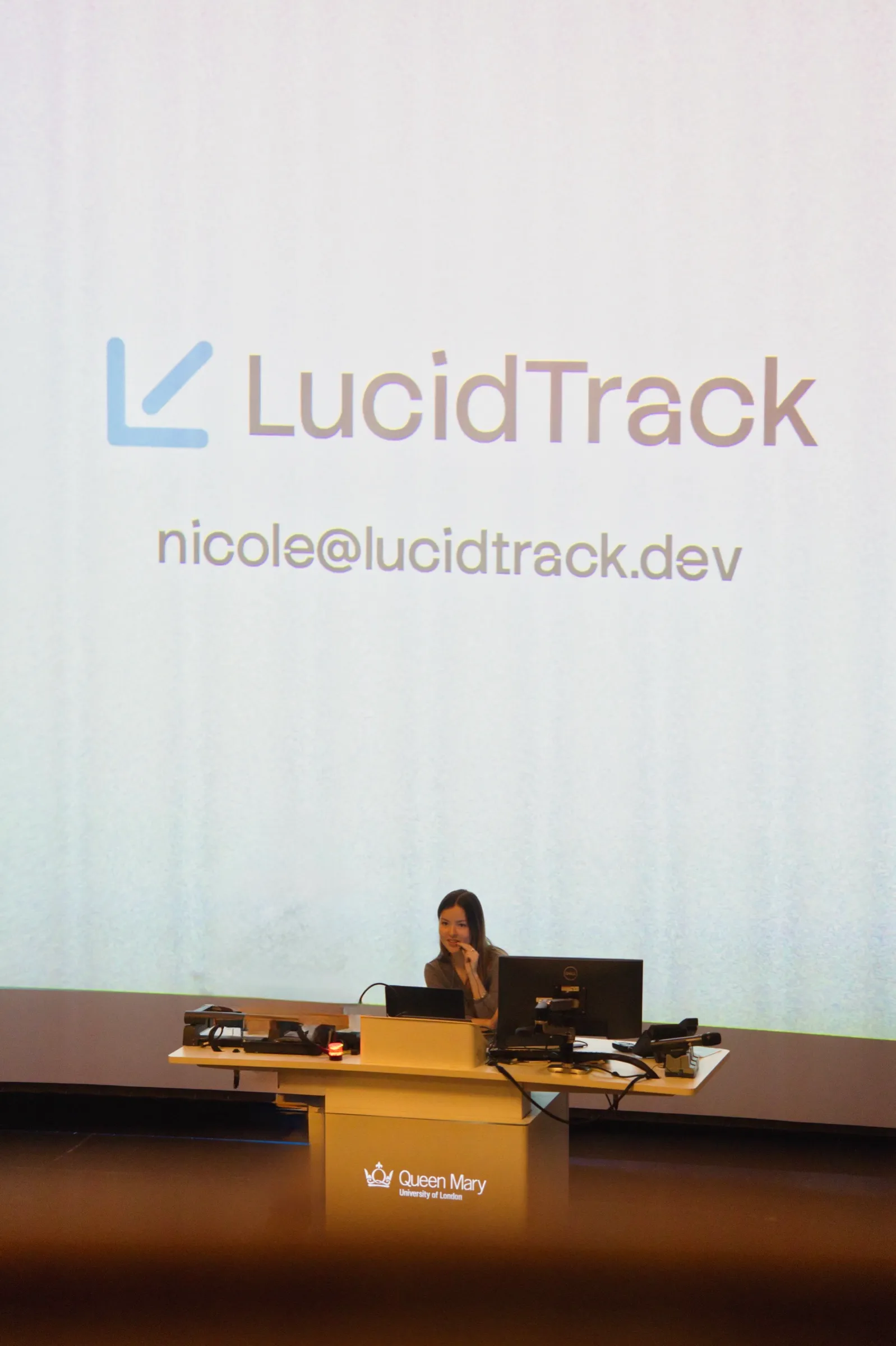 Me at the lectern in a Queen Mary lecture theatre, with LucidTrack on the screen behind her.
