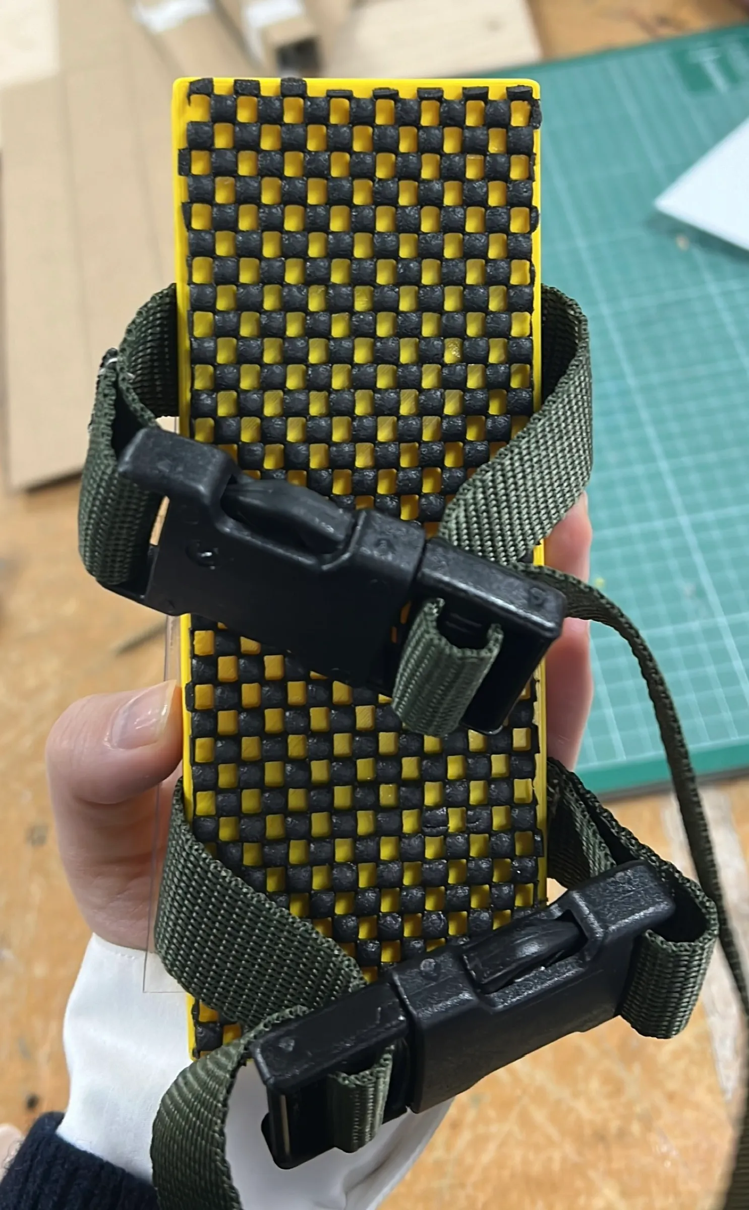The underside of the housing, held in a hand, with two green straps and black plastic clips around it.