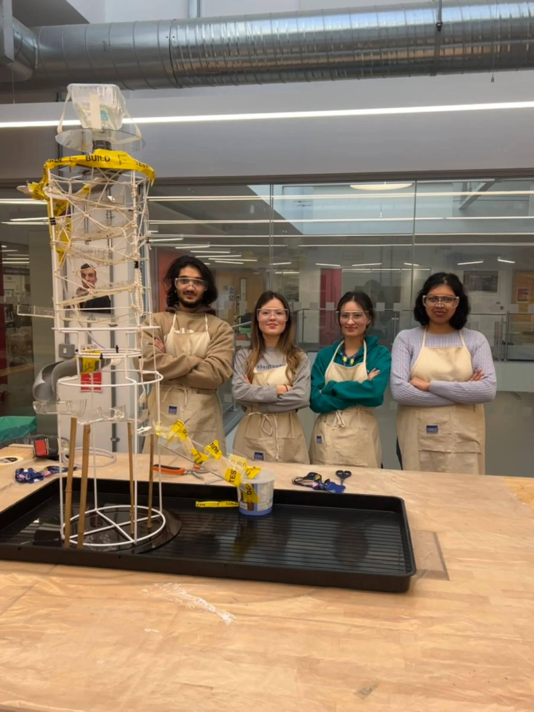 The four team members in workshop aprons, standing beside the finished tower.