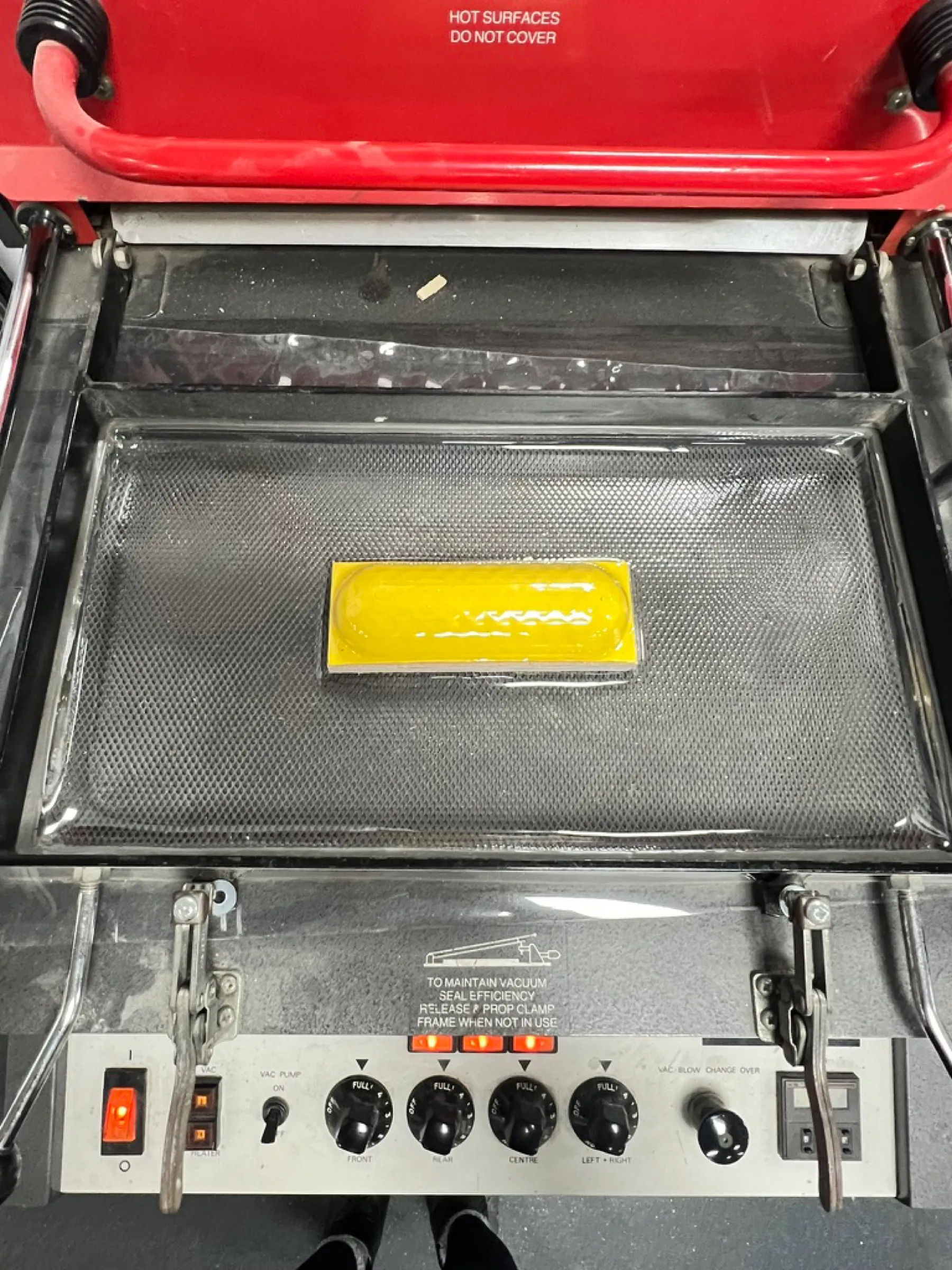 The yellow housing on the bed of a vacuum forming machine, under a sheet of clear plastic.